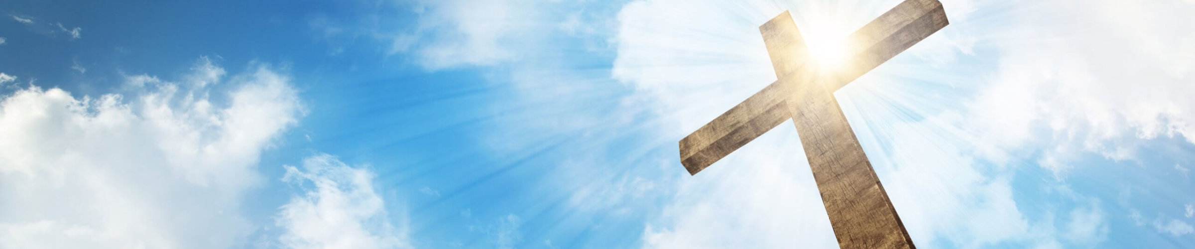 A wooden Christian cross with bright sun and clouds.